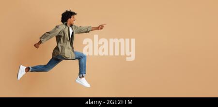 Look There. Overjoyed black guy pointing aside while jumping up in air Stock Photo