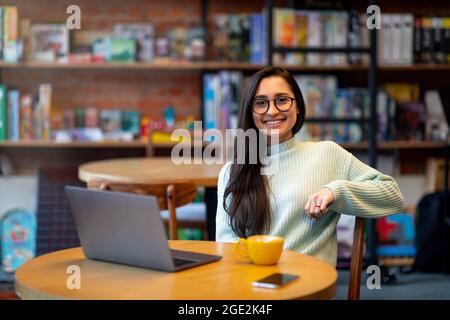 Excited arab female freelancer working distantly while sitting in cafe and using laptop computer, free space Stock Photo