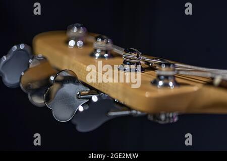 Detail of a tuning post on the wooden headstock of an electric bass guitar. Stock Photo