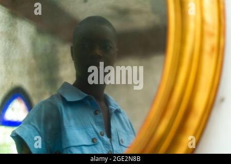 Short-haired black female looking at herself in the vintage gold framed mirror hung on white wall Stock Photo