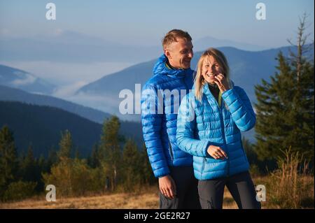 Couple of hikers sincerely laughing while resting in the mountains. Cheerful vacation in nature on background of misty mountain beskids. Concept of hiking, travelling and relationships. Stock Photo