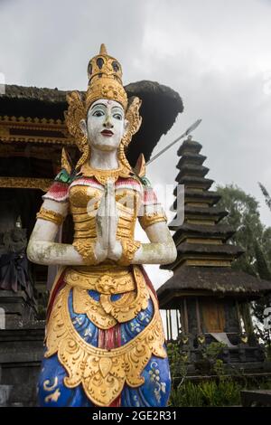 Colorful statue of a female goddess in the Ulun Danu Batur temple. Meru tower in the background. Bali, Indonesia. Stock Photo