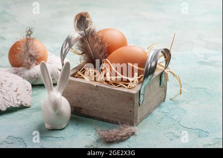 Easter composition with decorative rabbit, eggs and feathers on blue concrete background Stock Photo