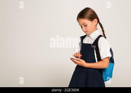 girl in school uniform messaging on mobile phone isolated on grey Stock Photo