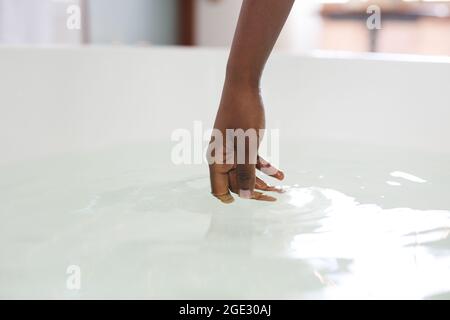 Close up of hand of african american woman in bathroom touching water in bath Stock Photo