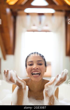 Portrait of laughing mixed race woman in bathroom having a bath Stock Photo