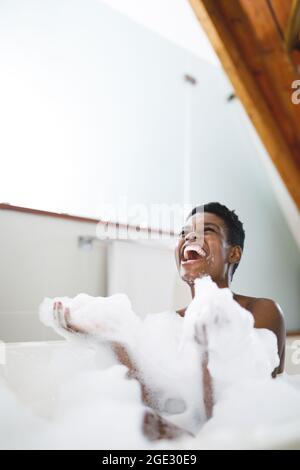 Happy african american woman laughing in bath, having fun with bath foam Stock Photo