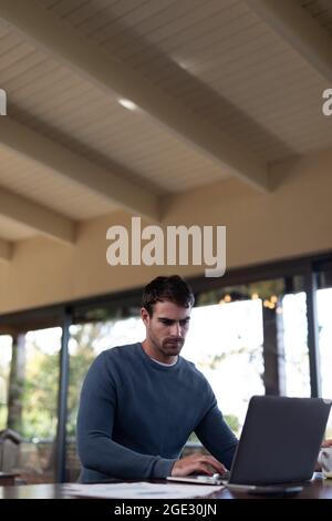 Caucasian man sitting at table and working remotely using laptop Stock Photo