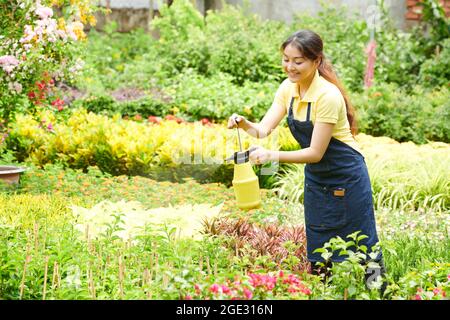 Pretty smiling young gardening center worker spraying and watering blooming flowers Stock Photo
