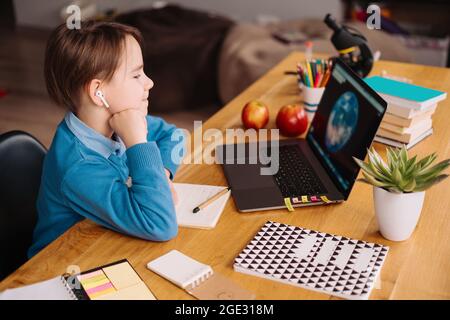 A Preteen boy uses a laptop to make online classes, globe on the screen, making notes Stock Photo