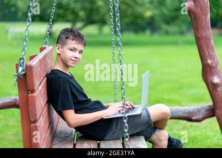 Boy with using laptop on the swing. First time to school. Outdoor learning concept Stock Photo