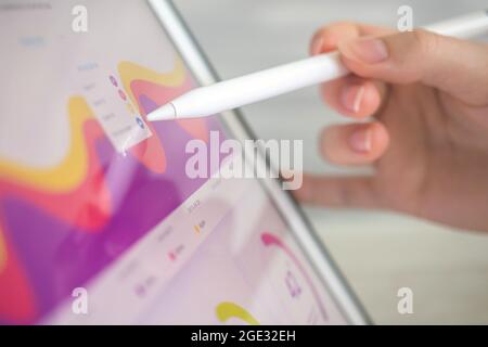 Business diagram on the screen, office desk background. Female worker analyzing financial results on digital tablet using wireless stylus Stock Photo