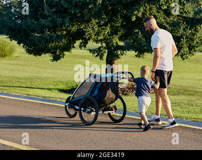 Father with his little son are walking in city park together and pushing a baby carriage. Fatherhood, daddy and child. father's day Stock Photo