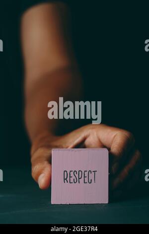 closeup of a young caucasian man showing a pinkish violet building block with the text respect written in it, on a dark gray surface Stock Photo