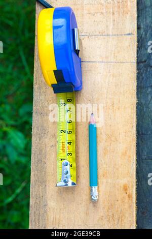 Construction measuring tape, pencil for marking on a wooden board. Wood construction concept. Vertical photography. Stock Photo