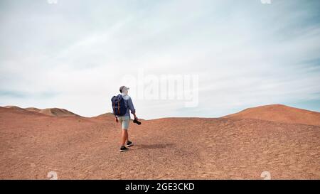 asian male backpacker landscape photographer walking on a hill looking at view, rear view Stock Photo