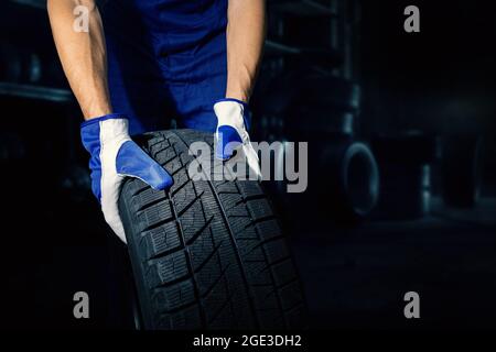 mechanic holding car tire on dark workshop background with copy space. tyre service Stock Photo