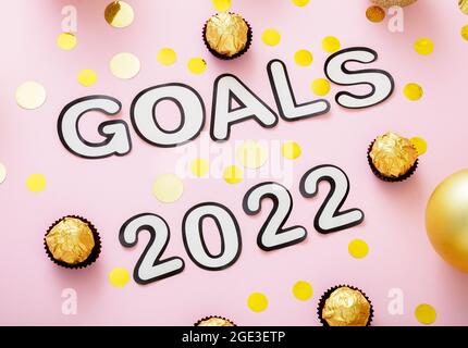 Goals 2022 lettering in Happy New Year style. 2020 Goals text with Christmas decorations gold confetti on pink color background. Stock Photo