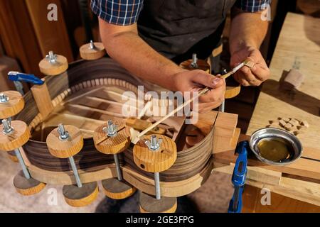 Unrecognized luthier creating a guitar and using tools in a traditional workshop. Stock Photo