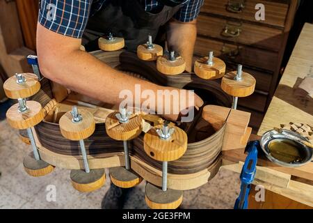Unrecognized craftsman creating a guitar and using tools in a traditional workshop. Stock Photo