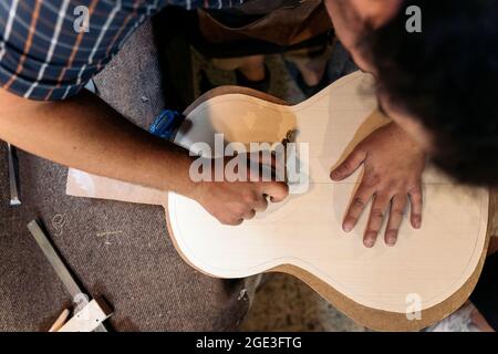 Unrecognized luthier working in his atelier and making a guitar. He is using a special tools. Stock Photo