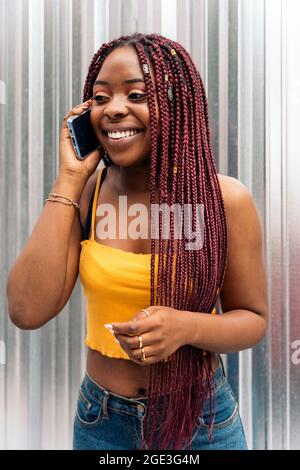 Cheerful young african woman with braids standing in the street and talking on the phone. Stock Photo
