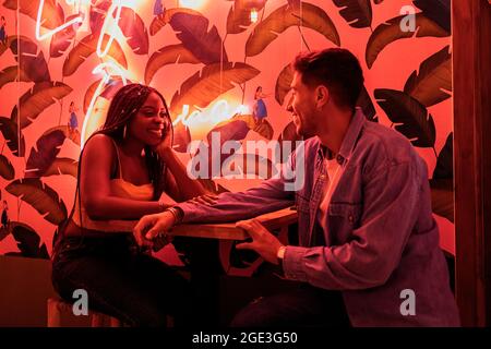 Pretty african woman with braids sitting in a restaurant with her boyfriend against cool lights. Stock Photo