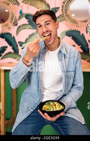 Handsome young man sitting in a restaurant enjoying a healthy poke bowl and looking at camera. Stock Photo
