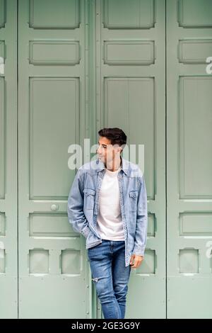 Cool young man wearing casual clothes smiling and looking to the side against green wall. Stock Photo