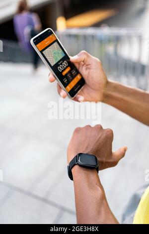 Close-up view of hands of African American man with yellow t-shirt synchronizing mobile phone and smartwatch to do sports in the city. Stock Photo