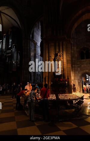 Freiburg, Germany. 16th Aug, 2021. Visitors to Freiburg Cathedral light candles while other visitors can be seen in the background. Freiburg Cathedral is formally a cathedral, as Freiburg has been an episcopal see since 1827. The Archdiocese of Freiburg was formally established on August 16, 1821 by Pope Pius VII through the bull 'Provida solersque'. Credit: Philipp von Ditfurth/dpa/Alamy Live News Stock Photo