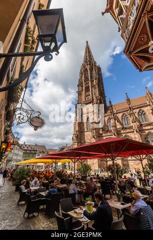 Freiburg, Germany. 16th Aug, 2021. People sit in a restaurant on Freiburg's Münsterplatz while the cathedral can be seen in the background. Freiburg Cathedral is formally a cathedral, as Freiburg has been an episcopal see since 1827. The Archdiocese of Freiburg was formally established on August 16, 1821 by Pope Pius VII with the bull 'Provida solersque'. Credit: Philipp von Ditfurth/dpa/Alamy Live News Stock Photo