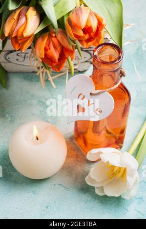 Spring composition with orange tulips in wooden basket, bottle and heart, lit cadle. Holiday, valentine's, mother's day Stock Photo