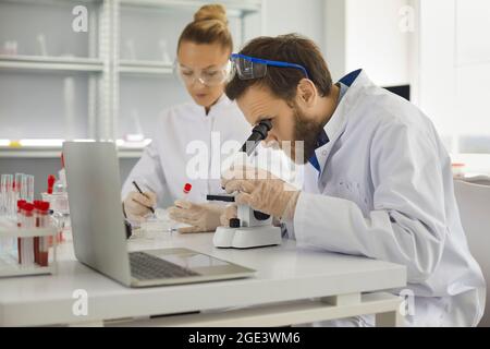 Research scientists lab experts working with blood test sample and microscope Stock Photo