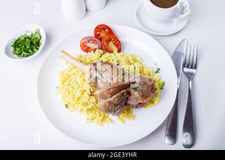 Lamb shin (shank) with rice, parsley, tomatoes and sauce on a white plate. Traditional dish. Close-up. Stock Photo