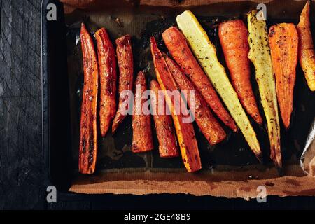 Roasted carrots in roasting tin on a dark wooden background. Stock Photo