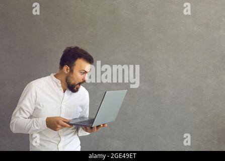 Young man shocked and surprised, looks at the laptop screen. Stock Photo