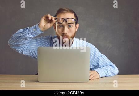 Surprised worker takes off glasses and looks at something shocking happening in office Stock Photo