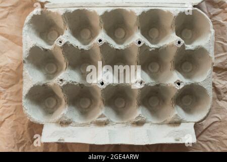 Opened empty egg cardboard box isolated on crumpled kraft paper background. Organic chicken egg carton pack or egg container top view. Stock Photo