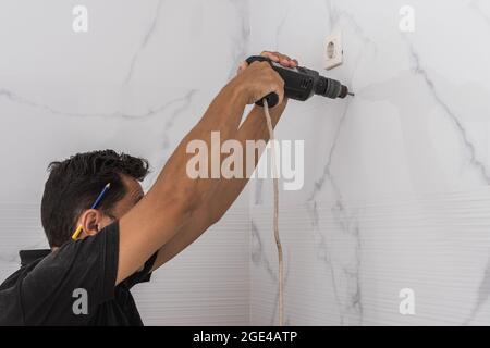 Man drilling a hole in a kitchen wall Stock Photo