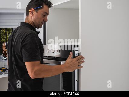 Man placing an oven inside the hole of a new kitchen cabinet Stock Photo