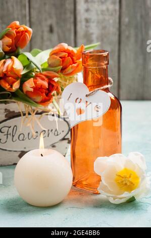 Spring composition with orange tulips in wooden basket, bottle and heart, lit cadle. Holiday, valentine's, mother's day Stock Photo