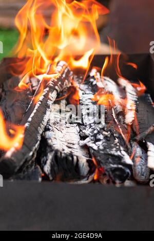 Metal brazier with burning wood and coals in nature on a bright summer sunny day. Bonfire with red flames. Selective focus. Close-up Stock Photo