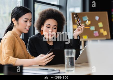 interracial businesswomen looking at clipboard while working in office Stock Photo