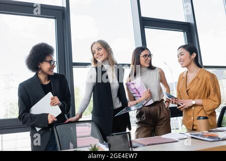 happy multiethnic businesspeople smiling at each other while talking in office Stock Photo