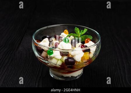 Salad from grapes apples pears kiwi oranges with mascarpone chease and cream. Healthy fresh fruit summer salad in glass bowl on black wooden backgroun Stock Photo