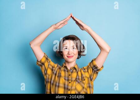 Photo of curious lady raise hands show roof form look up empty space wear checkered shirt isolated blue color background Stock Photo