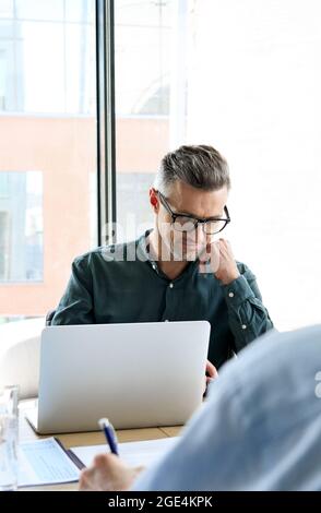 Serious male ceo looking at laptop near panoramic window at table meeting. Stock Photo