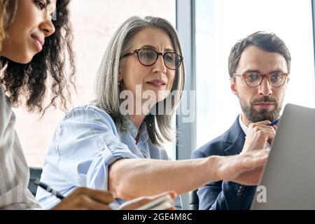Diverse business executive team discuss corporate report using laptop at table. Stock Photo