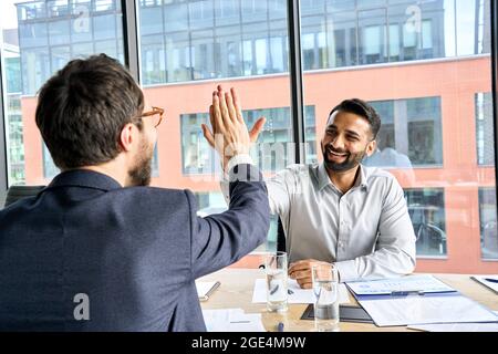 Two happy diverse professional businessmen giving high five at meeting. Stock Photo